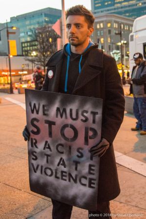 Protestor holding a 'We Must Stop Racist State Violence' Sign