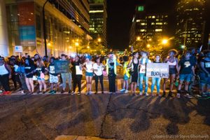 Protesters link arms and stand together along one of the crosswalks on the road