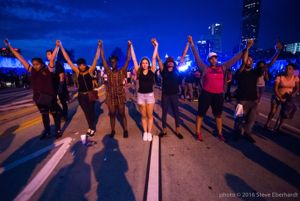 Protesters stand together in a line as they lock hands and hold them up in the air