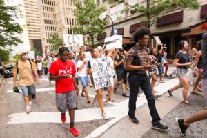 Protesters march down the street holding their hands and peace signs in the air