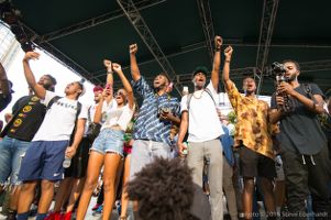 Protesters stand on a stage all holding their fists in the air as they chant