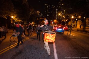 A protester marches through the streets playing a drum