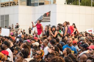Protesters sitting and standing on top of a stuck car point fingers and cry out