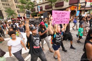 Protesters march down the street holding signs and their phones in the air