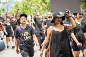 Protesters march through the streets with taped mouths and fists and signs held in the air