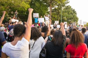 A crowd of protesters hold up their fists while listening to a speech given by Mawuli Davis