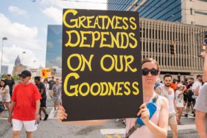 A protester holds up a sign reading 'Greatness Depends on Our Goodness'