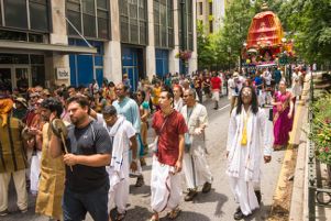 Participants walk in front of an ornate cart, some playing instruments