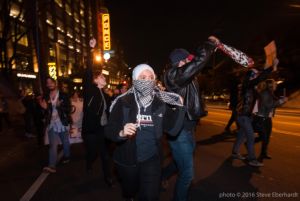 Protesters march through the streets with hands in the air and covered faces