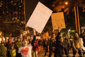 Protesters marching through the streets carrying signs reading off things protesters would not stand for