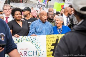 Representative John Lewis, Stacey Abrams, and other protesters hold up a large banner while marching