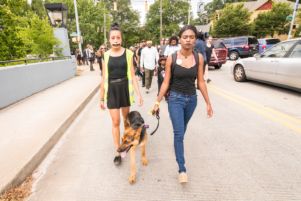 A protester with a taped mouth marches alongside another who has her dog with her