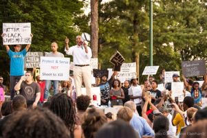 Mawuli Davis speaks to a crowd while signs are held up around them