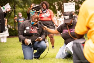 A protester pours a water bottle out onto the grass while giving a speech