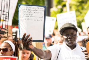 A protester holds up a sign with a handwritten note attached to the sign