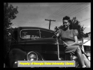 Ellen Lennox sitting on the front bumper of a 1938 Ford, Atlanta, Georgia, circa late 1930s or early 1940s