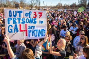 A protester holds up a sign reading 'Out of 37 Prisons in GA 4 are private'
