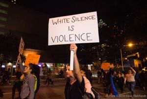 A protester holds up a sign reading 'White Silence is Violence'