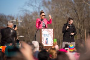 Alyssa Milano holds up her hand to point at the crowd while giving a speech