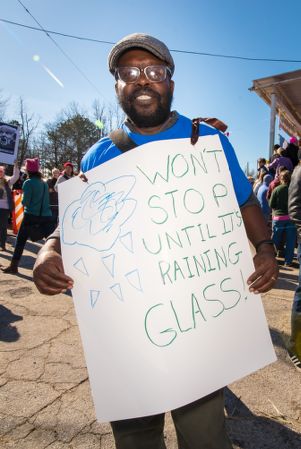 A protester wears a sign around his neck reading 'Won't Stop Until It's Raining Glass'