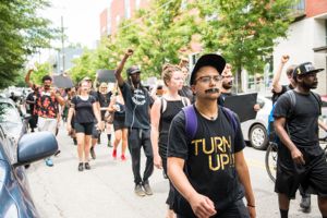 Protesters dressed in all black with tape over their mouths march down the street