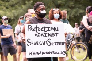 A protester holds up a sign reading 'Protection Against Search and Seizure'