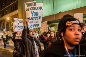 A protester marches while holding a 'Youth of Colot, You Matter and are Loved' sign