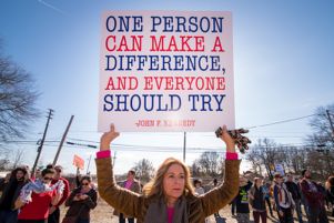 A woman holds up a sign featuring a John F. Kennedy quote