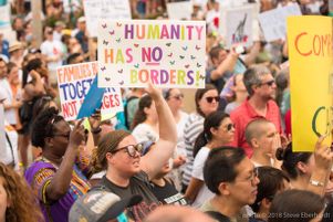 A protester holds up a colorful sign reading 'Humanity has No Borders'