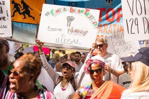 A protester holds up a sign above the crowd reading '#FamiliesBelongTogether Because Nobody is Illegal'
