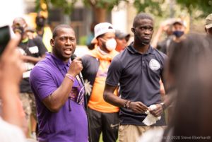 A protester in a purple shirt speaks to other protesters using a microphone