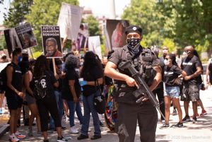 A protester dressed in police gear and holding a model weapon marches at the front of the protest