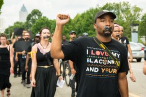A protesters with black tape over their mouth holds a fist in the air