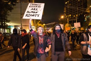 A protester holds up a sign reading 'Trans Rights are Human Rights' while holding hands with another protester