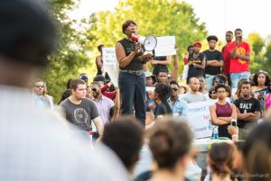 A woman gives a speech to crowd of protesters with signs