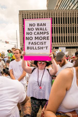 A protester holds up a large sign reading 'No Ban, No Wall, No Camps, No More Fascist Bullsh*t'