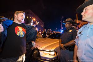 A protester shows his Fallout shirt to Police Officers while facing off with them