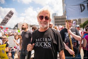 A protester stands amongst the crowd of protesters wearing a 'Racism Sucks' shirt