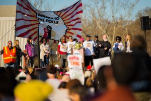 Protest organizers stand on the stage looking out at the crowd