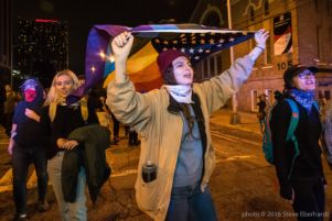 A protester carries an American Flag where the stripes are a rainbow pride flag