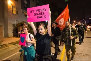 A protester marches through the streets holding up a sign reading 'My Pussy Grabs Back'