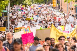 Protesters march together holding up a multitude of signs as they protest
