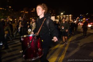 A protester marches through the streets playing a drum