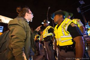 A protester points at and speaks to a Police Officer who gives no reaction