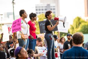 Protesters stand before the crowd while one gives a speech to the crowd