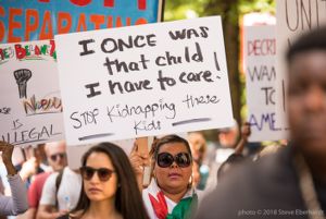A protester holds up a sign reading 'I Once Was That Child I have to Care! Stop Kidnapping these Kids'