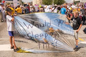 Two young protesters hold up a blanket reading 'Would you sleep on this?'