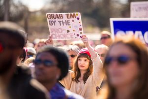 A protester wearing a pink hat holds a sign reading 'Grab 'Em by the Pro-Choice'