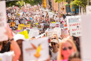 Protesters march together holding up a multitude of signs as they protest