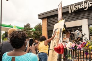 An artist paints a tribute to Rayshard Brooks while protestors join her by holding signs, Atlanta, GA